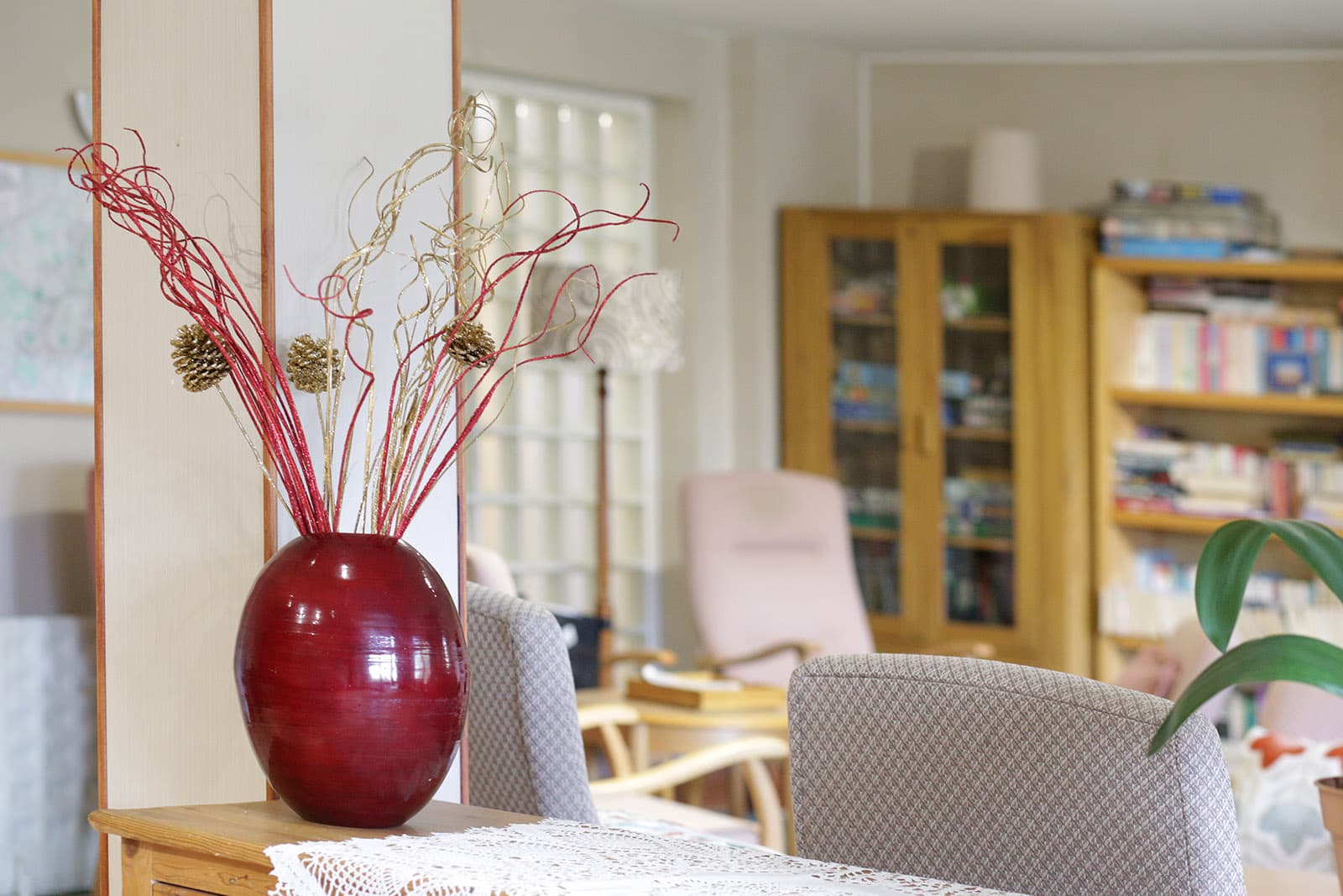 The communal lounge at Lloyd Court, with armchairs, bookshelves and a vase of dried flowers on a side table.