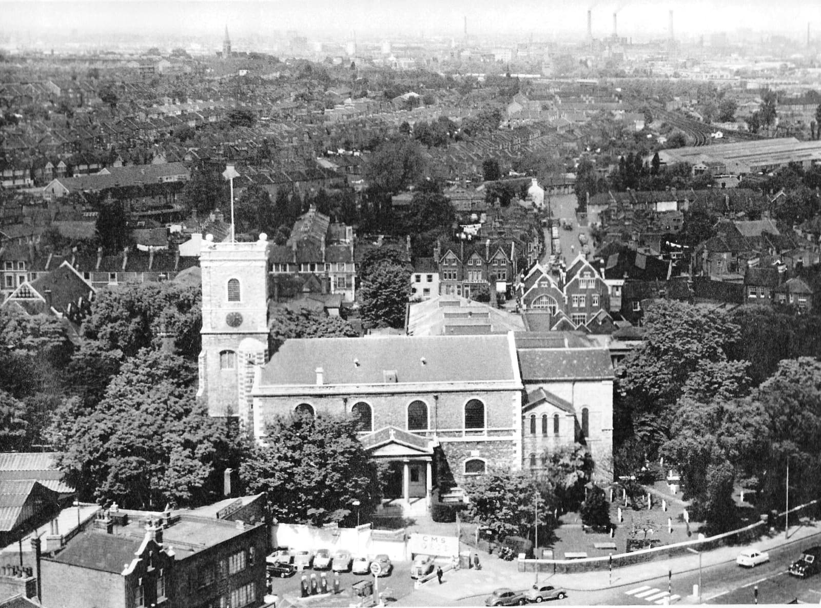 An aerial photograph of the church and churchyard surrounded by roads, houses and traffic.