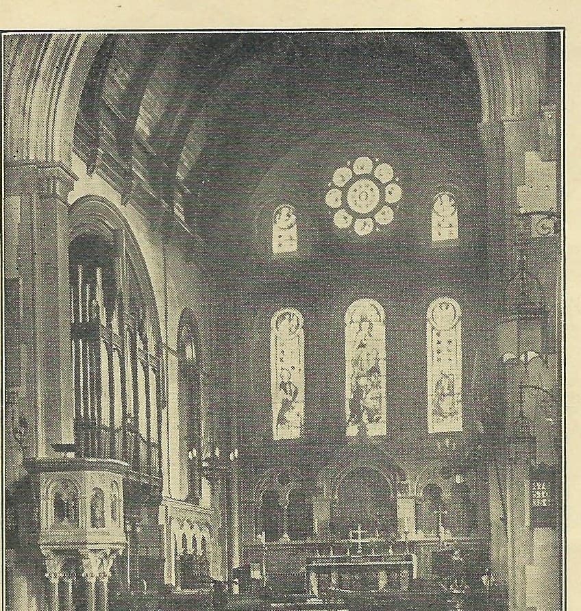 A photograph of the chancel in the 1920s, with the tall pipes of the Brindley and Foster organ filling the arch on the left, a stone pulpit below them, and the rose window and stained glass above the altar.