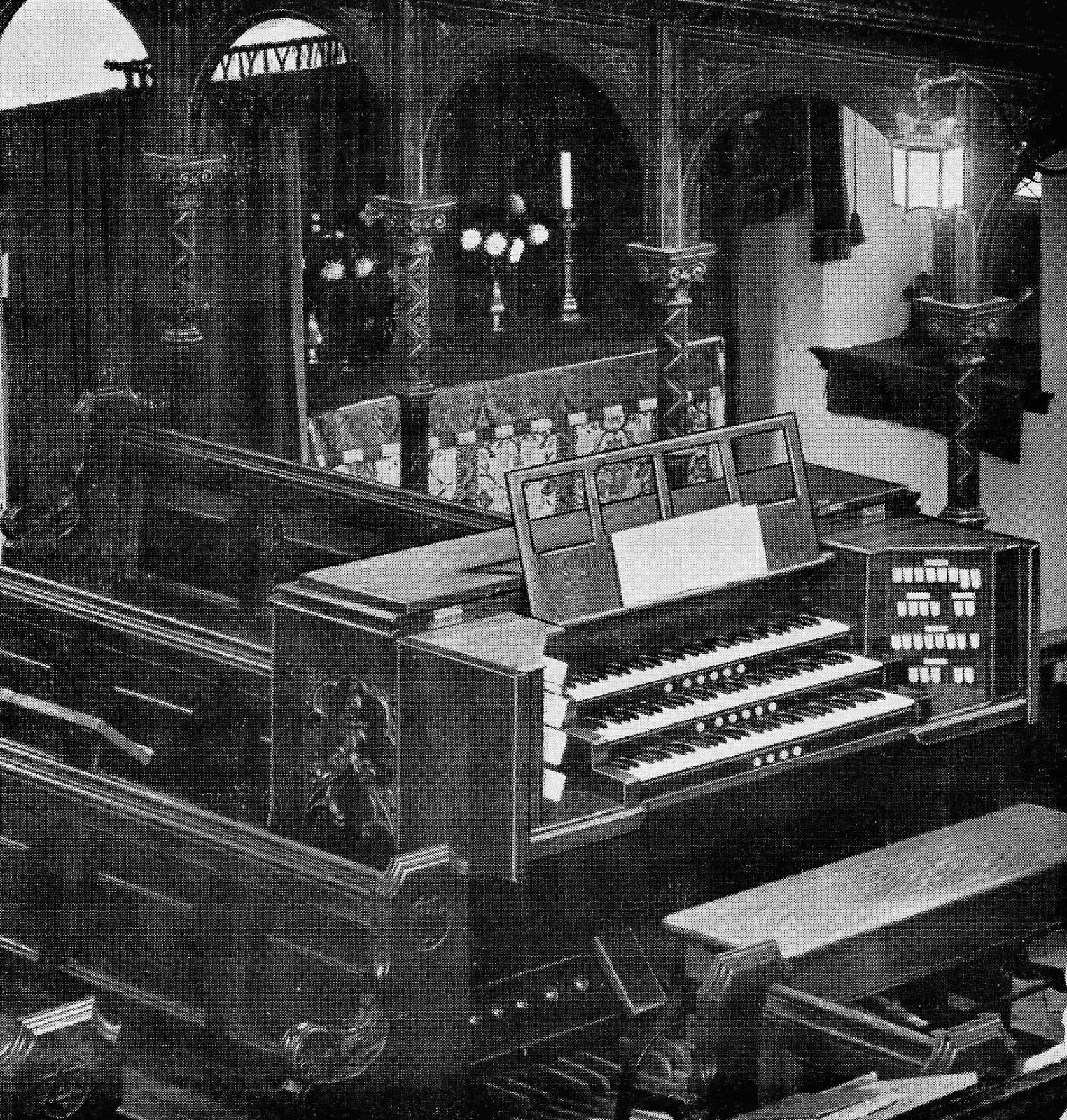 A three-manual organ console standing in the chancel, with stop tabs in stepped rows on the jamb to the right of the player.