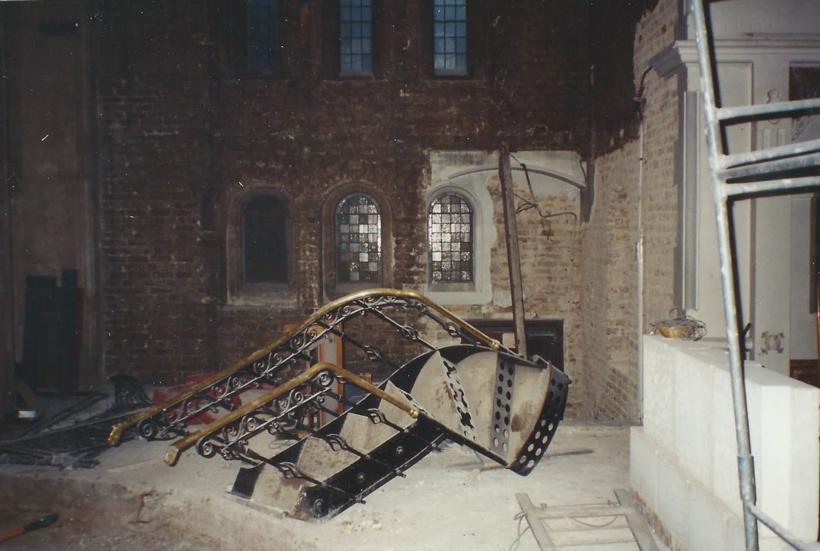 The wooden frame and casework of a dismantled organ, collapsed on the floor of a bare brick interior.