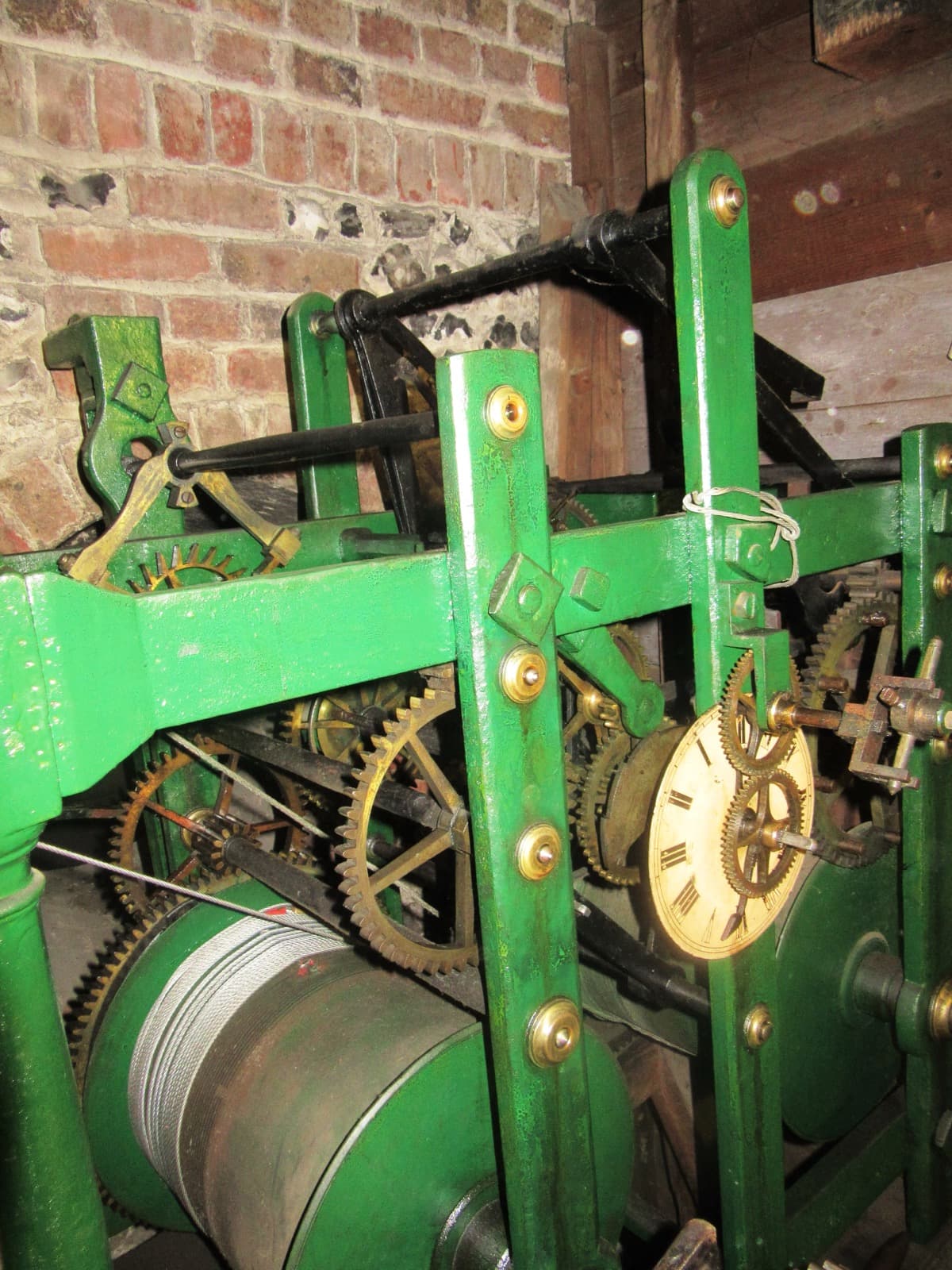 A cast-iron clock movement painted green, with brass gear wheels and a winding drum, standing in a stone chamber.