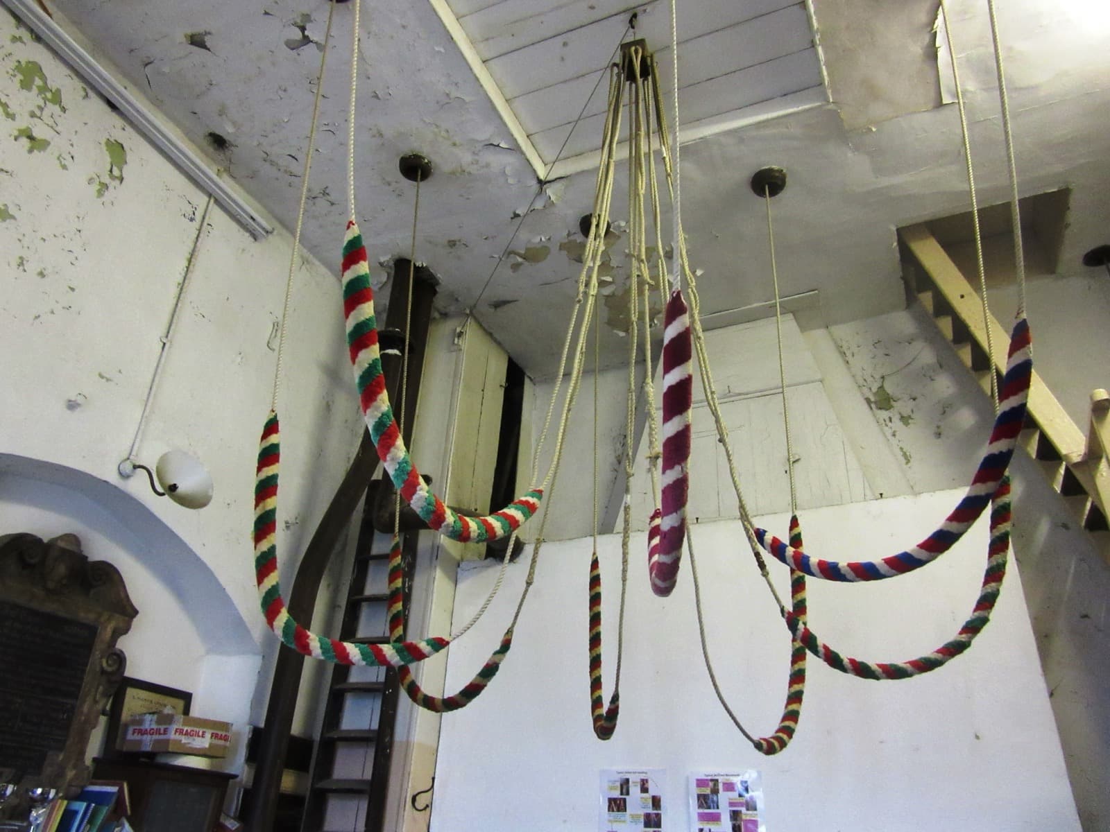 The ringing chamber, with eight bell ropes hanging in a circle, their striped woollen sallies at head height, and peal boards on the walls.