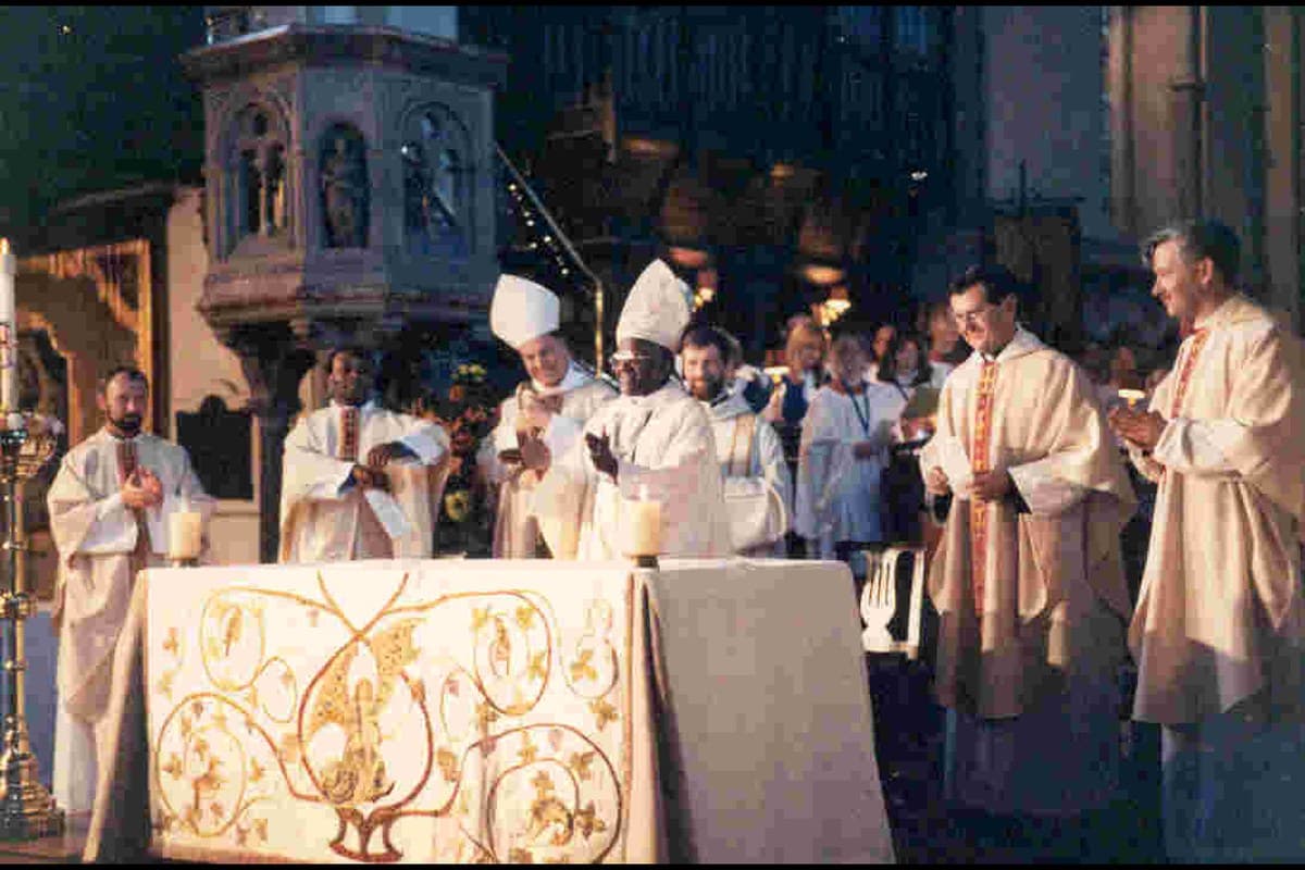 Archbishop Desmond Tutu, in a mitre, standing at the altar of St Mary's with another bishop and a group of concelebrating clergy and servers. The stone pulpit is behind them and the altar carries an embroidered frontal.