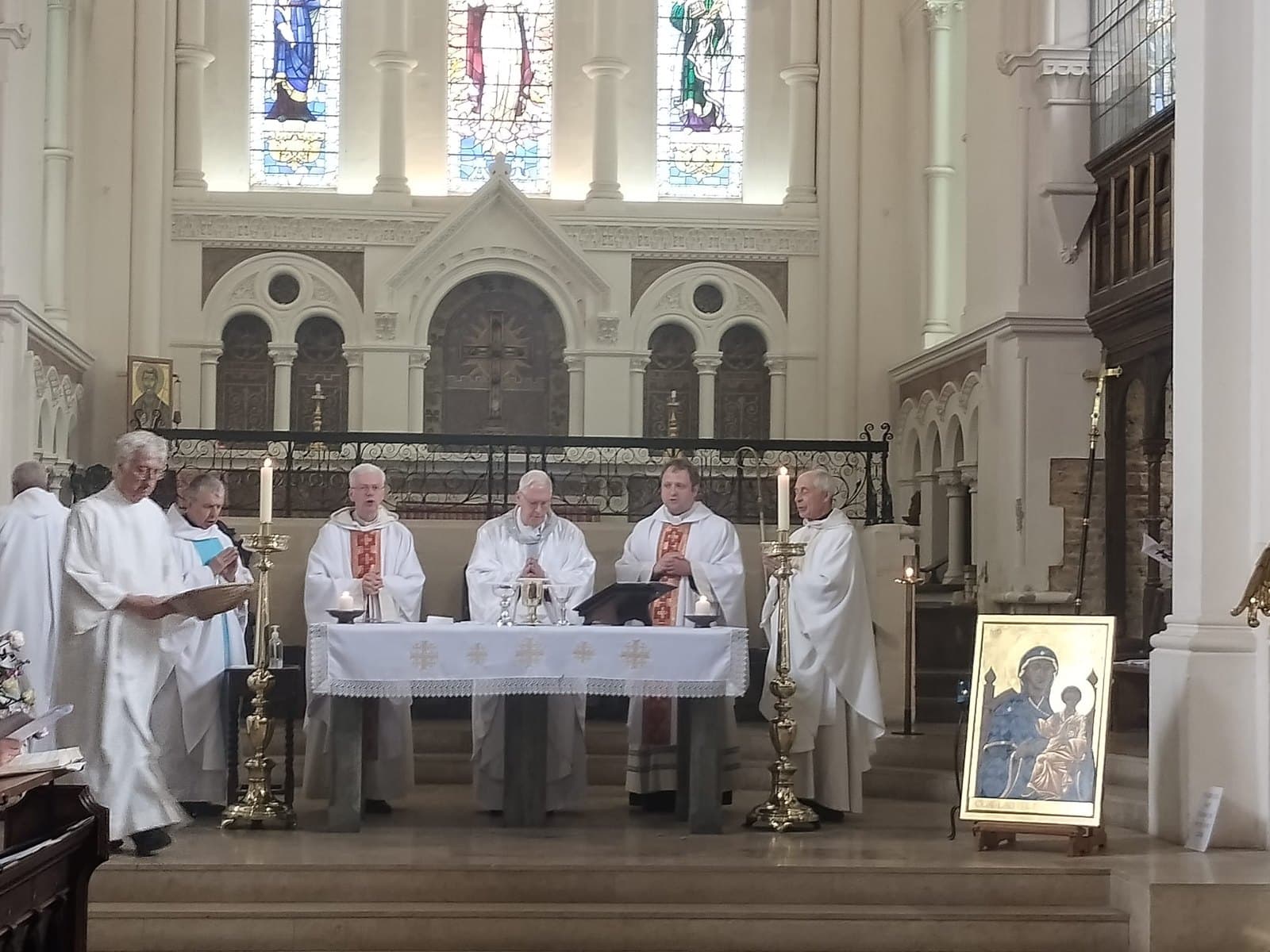 The Sung Mass at the high altar of St Mary's, three priests concelebrating with the bishop in the centre, servers to the left, and the icon of Our Lady of Lewisham standing on an easel at the right of the sanctuary steps.
