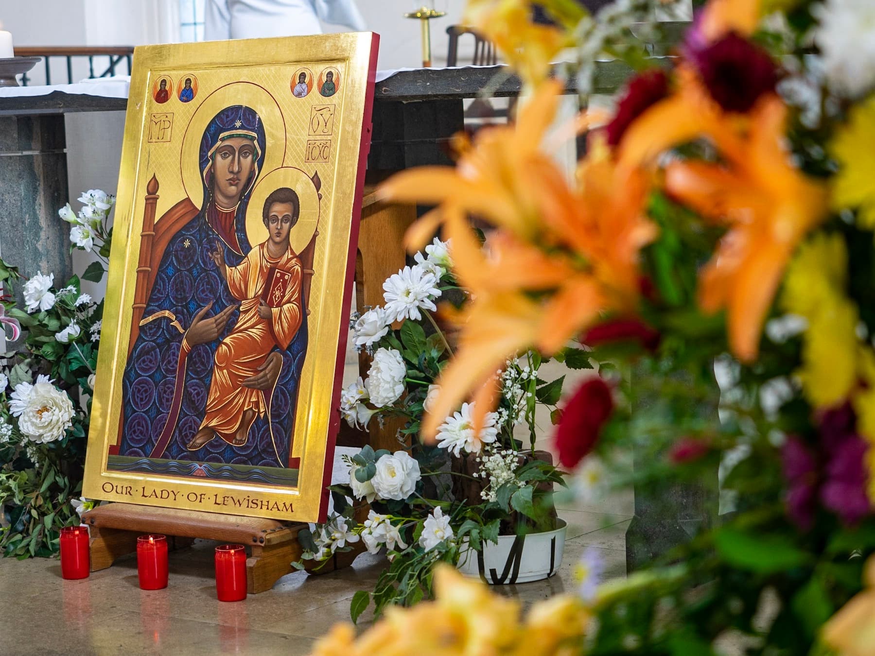 The icon of Our Lady of Lewisham, gilded, with candles burning before it and flowers in front.