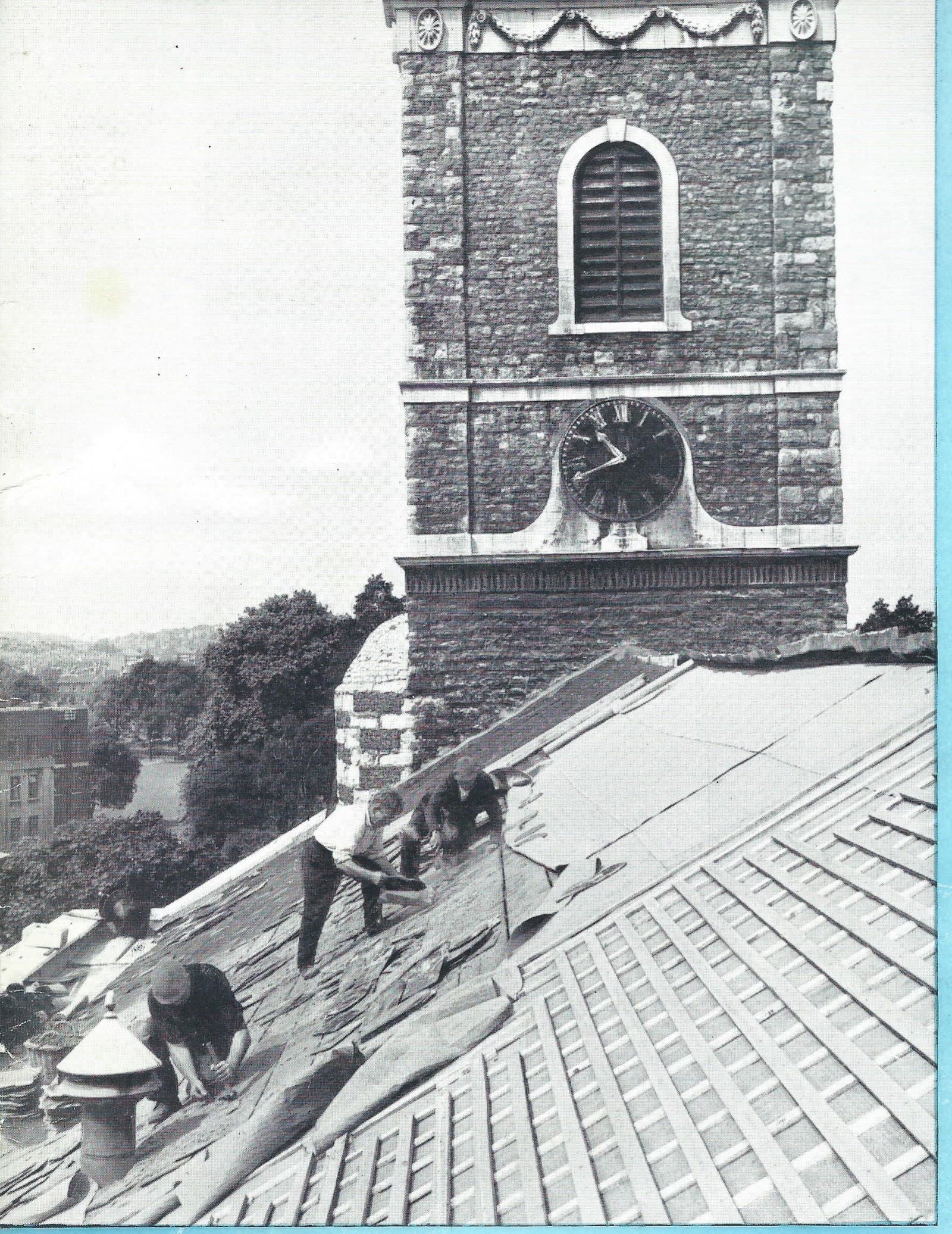 Four men stripping and re-laying the roof of the church in 1963, with the tower and its clock rising behind them and south London beyond.