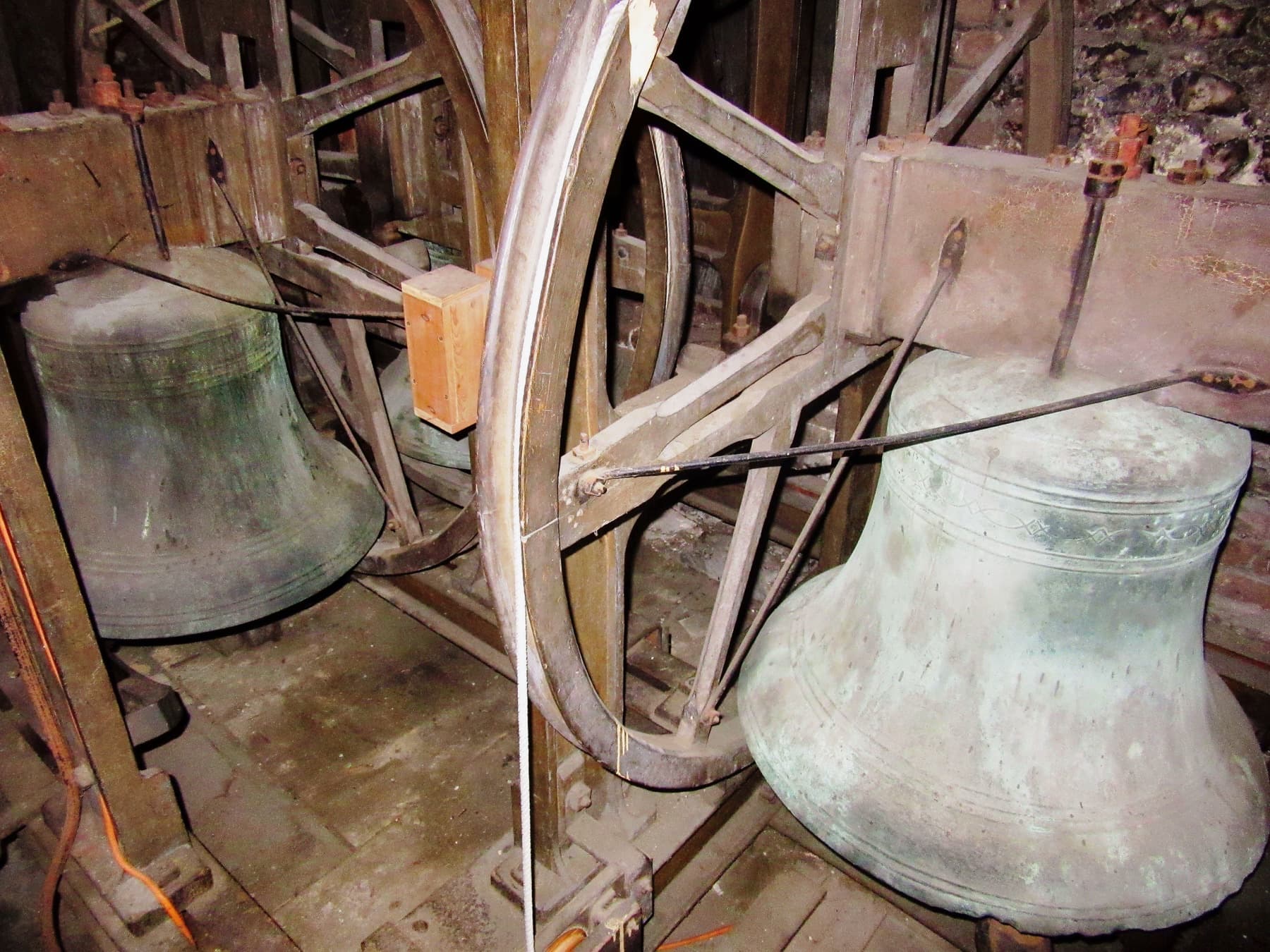 Two of the bells in their frame in the tower, mouths down, with the wheel and headstock of one visible above.